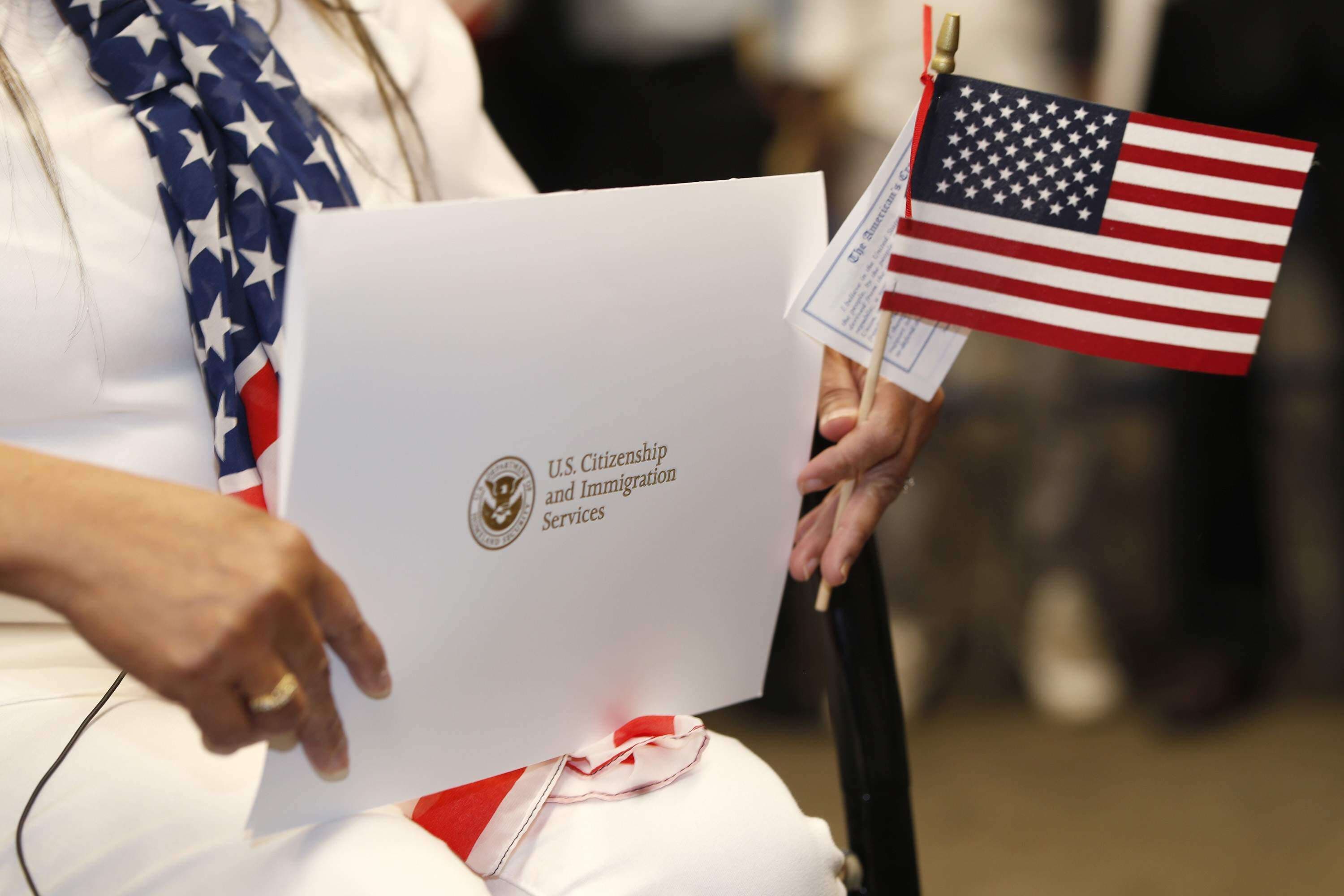 A person holding an American flag and a citizenship ceremony folder.