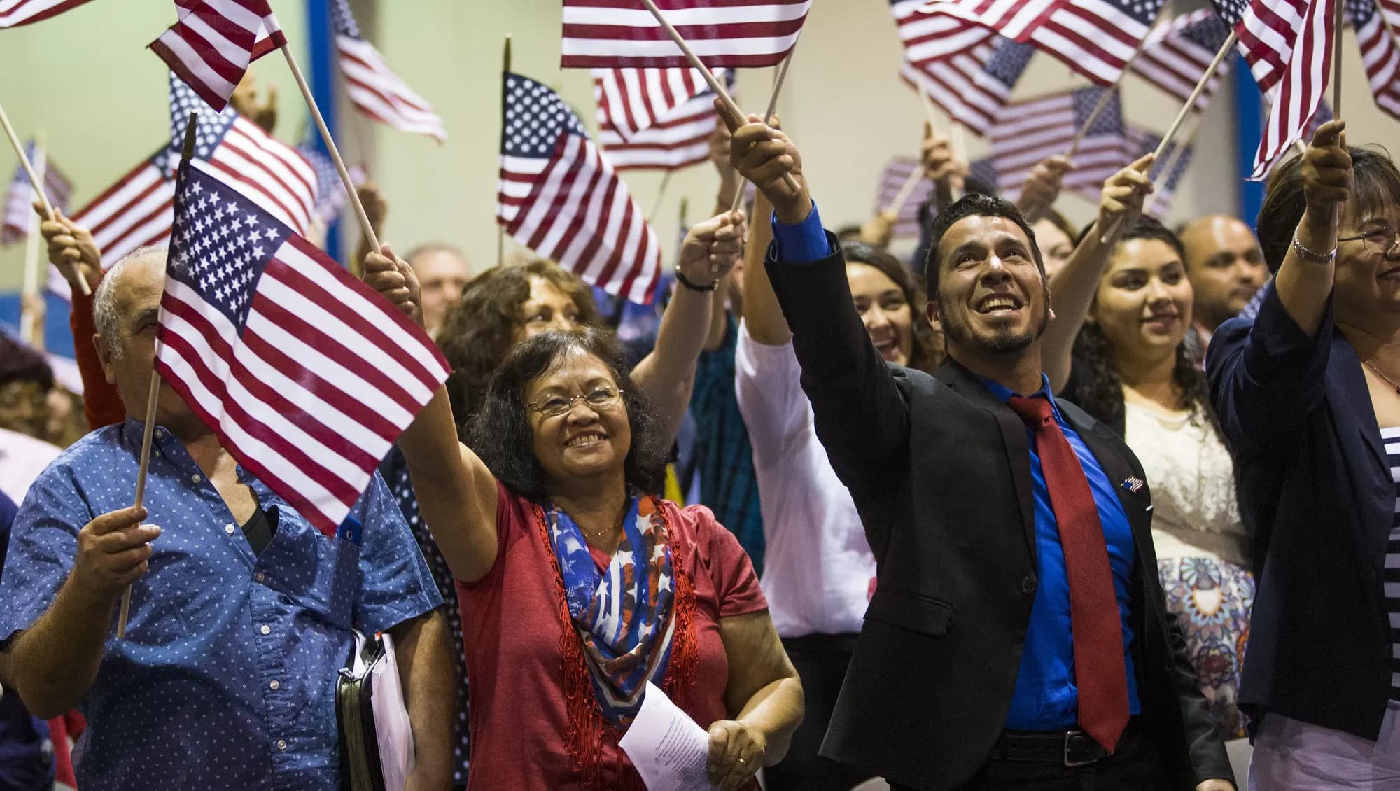 New citizens cheering and waving American flags after a naturalization ceremony.