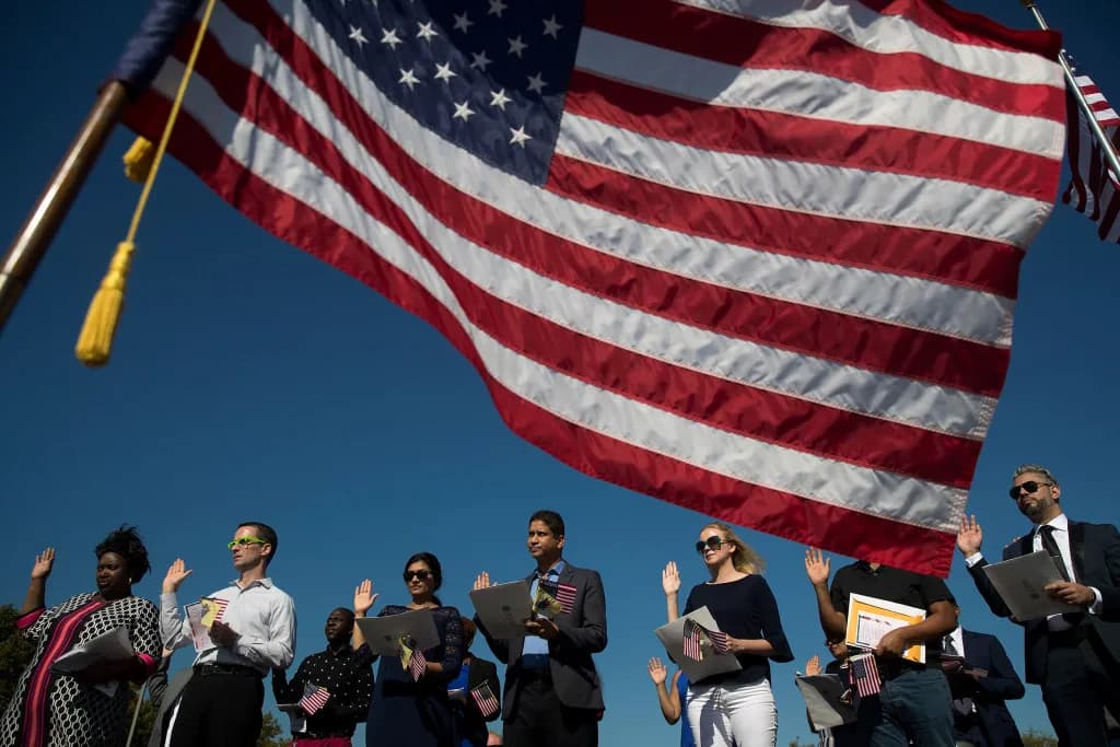 New citizens raising their right hands during the oath at an outdoor naturalization ceremony.